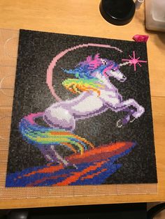 a cross stitch picture of a unicorn on a table