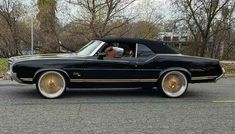 a black car with gold rims parked on the side of the road in front of some trees