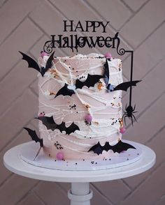 a halloween cake decorated with bats and sprinkles on a white pedestal in front of a brick wall