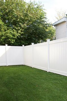 a white fence is in the grass next to a house