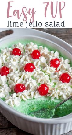 a green cake with cherries and whipped cream in a white dish on a wooden table