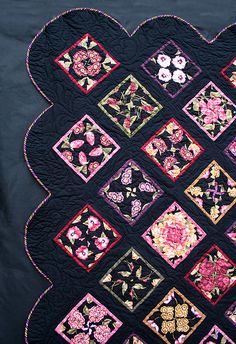 a black quilt with pink and yellow flowers on the center is displayed in front of a blue background