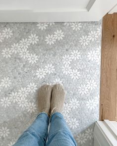 the feet of a person standing in front of a wall with white flowers on it