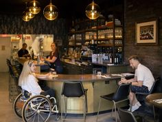 a woman in a wheelchair sitting at a bar with two other people behind the counter