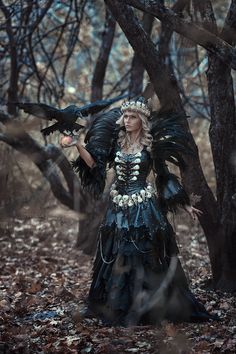 a woman dressed as a fairy holding a bird in her hand while standing next to a tree