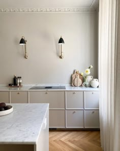 a white kitchen with marble counter tops and gold fixtures on the wall, along with wooden flooring