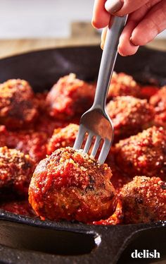 a person is holding a fork over meatballs in a skillet with tomato sauce