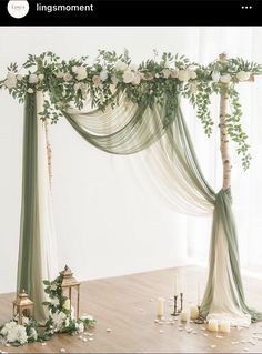 a wedding arch decorated with greenery and white flowers on the floor next to candles