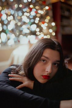 a woman with long hair and red lipstick is leaning on a couch in front of a christmas tree