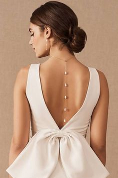 the back of a woman wearing a white dress with a large bow on it's neck