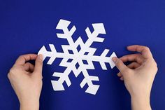 two hands are making a snowflake out of white paper on a blue background