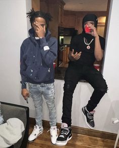 two young men standing next to each other in front of a mirror drinking from cups