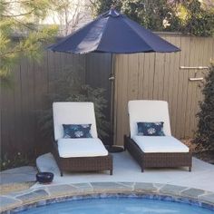 two lounge chairs sitting next to a swimming pool with an umbrella over the hot tub