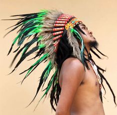 a man with feathers on his head is standing in front of a beige wall and looking up at the sky