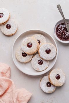 powdered sugar cookies and jam on a plate next to a bowl of fruit preserves