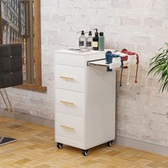 a white cabinet with three drawers in front of a brick wall and potted plant