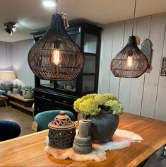 a wooden table topped with two vases filled with green plants and lights hanging from the ceiling