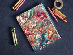 an open notebook with colored pencils and markers next to it on a blue surface