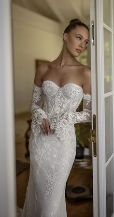 a woman in a white wedding dress is standing by the door and looking at the camera