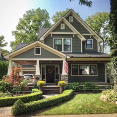 a gray house with an american flag on the front door and bushes in front of it