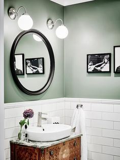 a bathroom with green walls and white tile on the floor, round mirror above sink