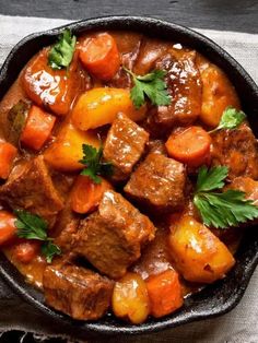 beef stew with carrots and parsley in a cast iron skillet on a table