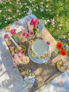 a table topped with a cake covered in frosting and flowers on top of a field