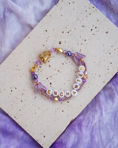 a purple bracelet with white beads and gold charms that says,'march'on it