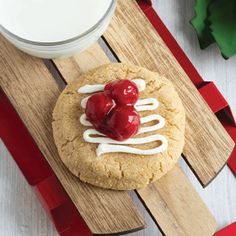 a cookie with two cherries on it next to a glass of milk