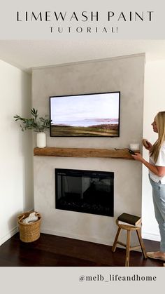 a woman standing in front of a flat screen tv mounted on a wall above a fireplace