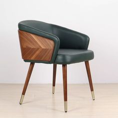 a green leather chair with wooden legs and arm rests on a hard wood floor in front of a white wall