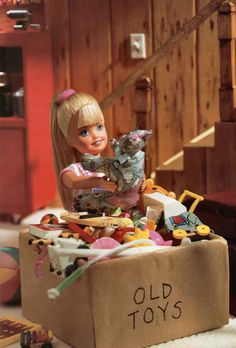 a doll is sitting in a cardboard box filled with toys