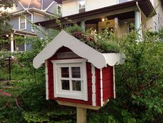 a red and white birdhouse sitting in front of a house with trees around it