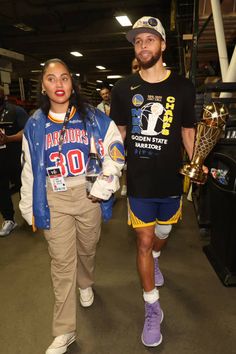 a man and woman walking down a hallway holding trophies in their hands while wearing matching shirts