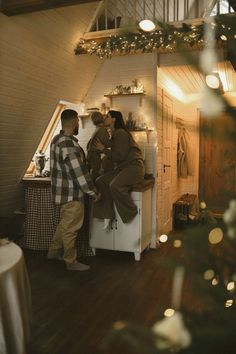 two people standing next to each other in front of an open refrigerator with christmas lights on the ceiling