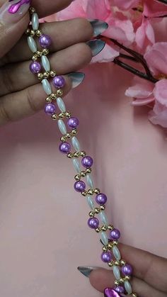 a woman holding onto a purple and white beaded bracelet with pink flowers in the background