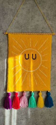 a yellow wall hanging with tassels and a smiley face drawn on the front