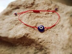 a red string bracelet with an evil eye bead on it sitting in the sand