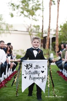 a little boy in a tuxedo holding a sign