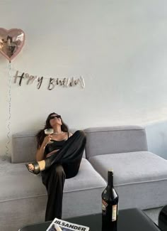 a woman sitting on top of a couch next to a bottle of wine and a balloon