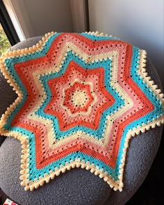 a crocheted blanket sitting on top of a gray chair next to a window