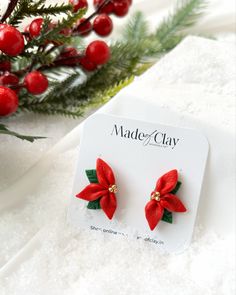 red poinsettia flower stud earrings with green leaves on white surface next to christmas tree