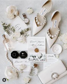 the wedding stationery is laid out with white flowers and shoes, jewelry, and perfume bottles