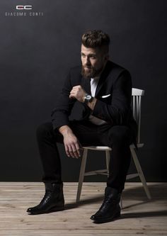 a man in a black suit sitting on a white chair