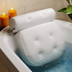 a white bath tub with candles on the side next to it and a plant in the corner