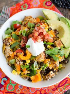 a white bowl filled with rice, vegetables and avocado on top of a colorful place mat