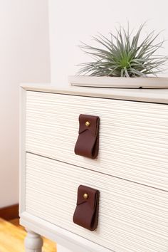 a white dresser with two brown handles and a potted plant on top