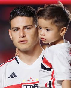 a man holding a little boy in his arms while wearing a soccer jersey with stars on it