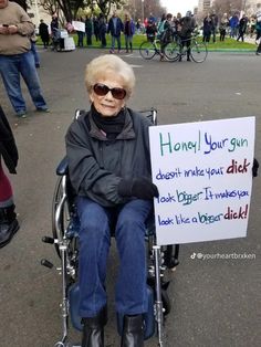 an elderly woman in a wheel chair holding a sign