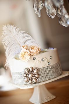 a white cake with feathers and flowers on it sitting on top of a wooden table